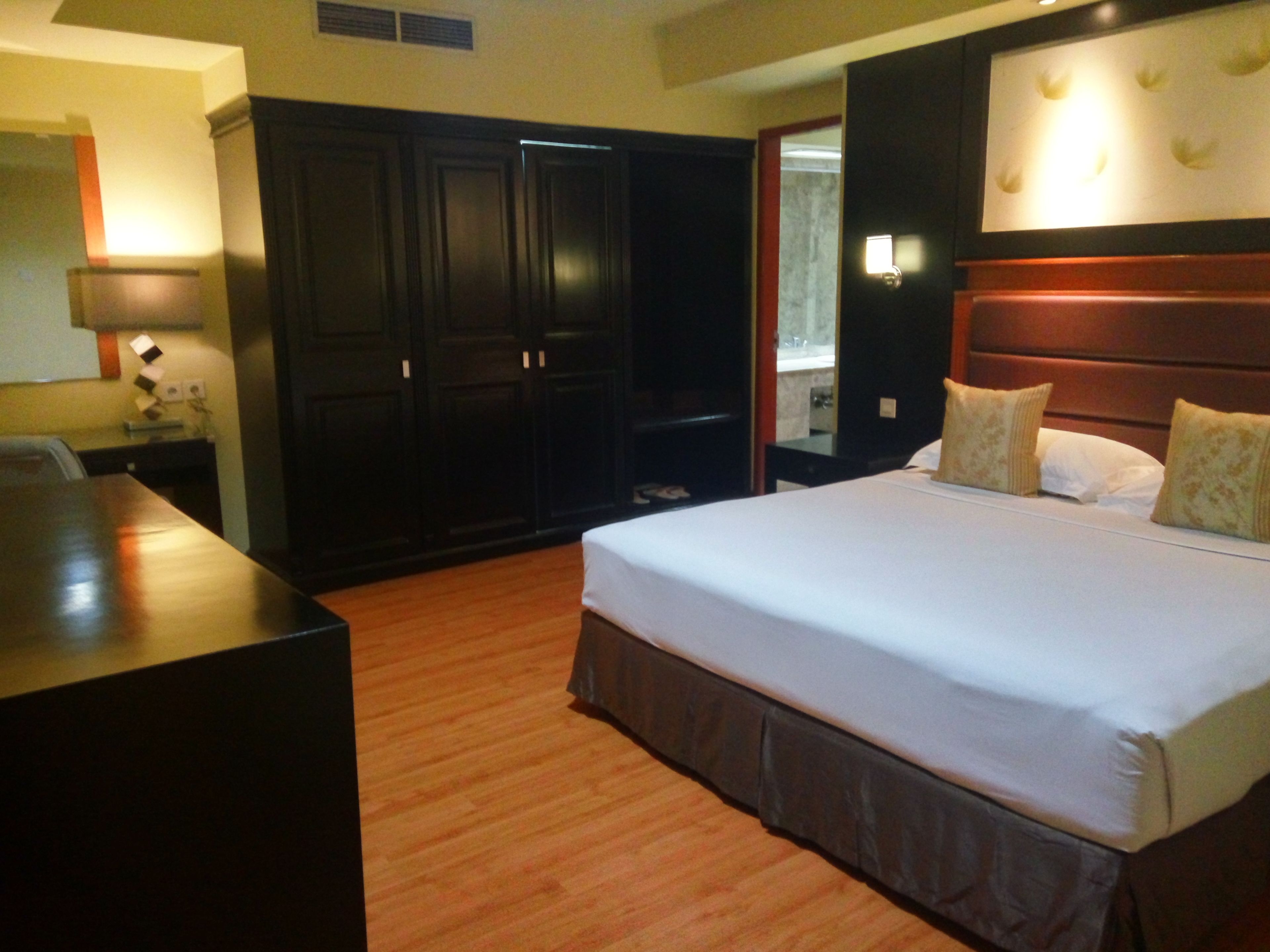 A hotel room with a large bed, a wooden desk, and dark wooden wardrobes.