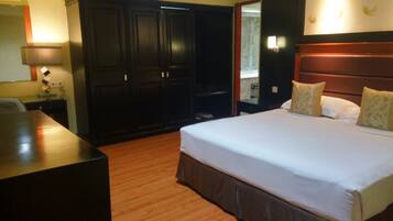 A hotel room with a large bed, a wooden desk, and dark wooden wardrobes.
