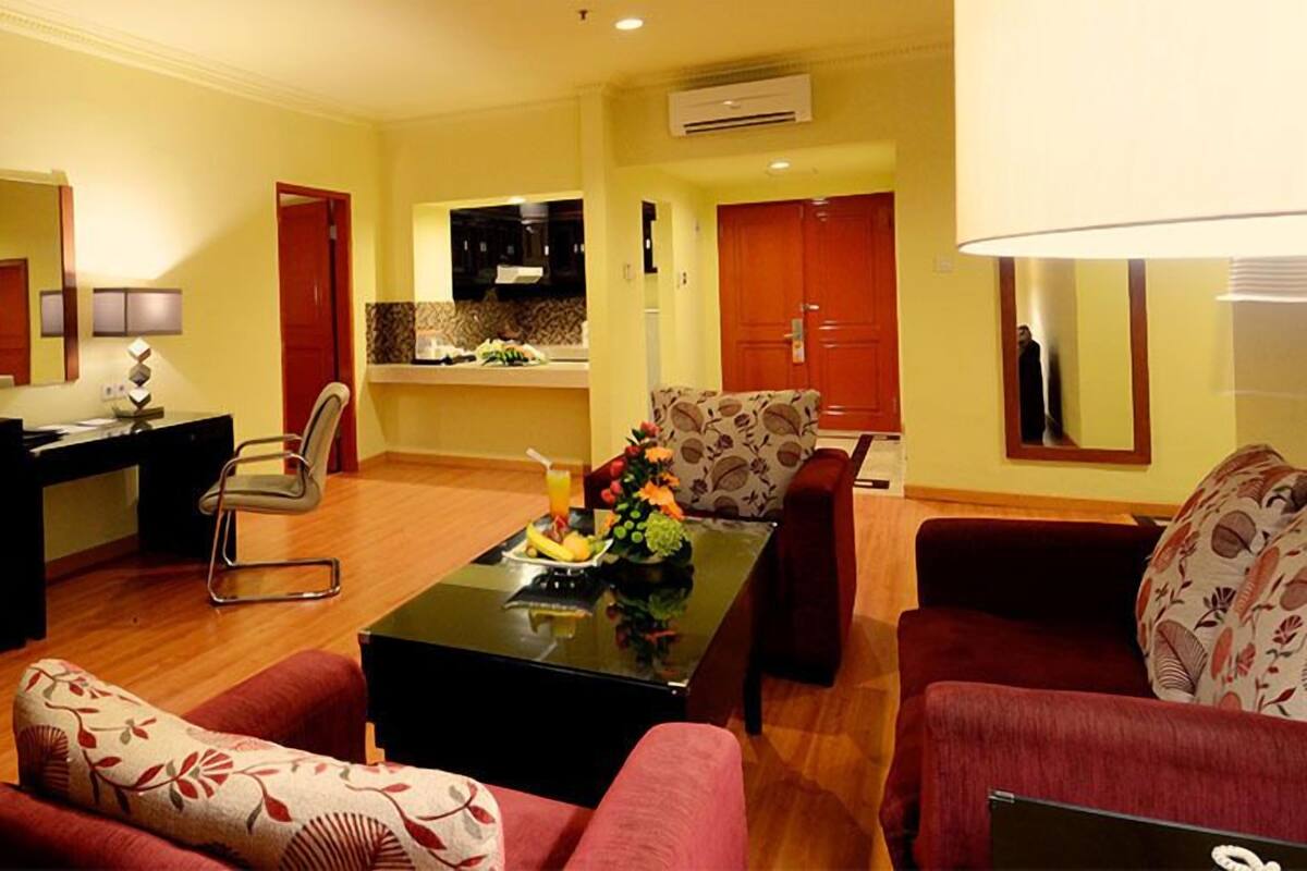 Una sala de estar con televisor, una mesa de comedor con fruta, un sofá y una zona de cocina al fondo.