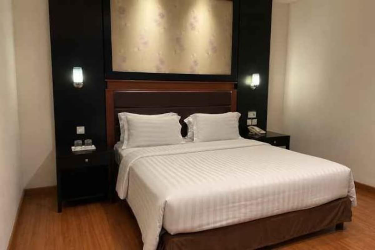 Een hotelkamer met een groot bed, een houten hoofdeinde, twee nachtkastjes en een wandlamp.