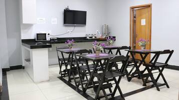 Una pequeña kitchenette con microondas, un lavamanos y un televisor de pantalla plana. Hay cuatro mesas con sillas, cada una con un pequeño jarrón de flores.