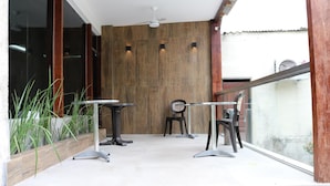 An outdoor seating area with two tables and chairs, a wooden wall, and a ceiling fan.