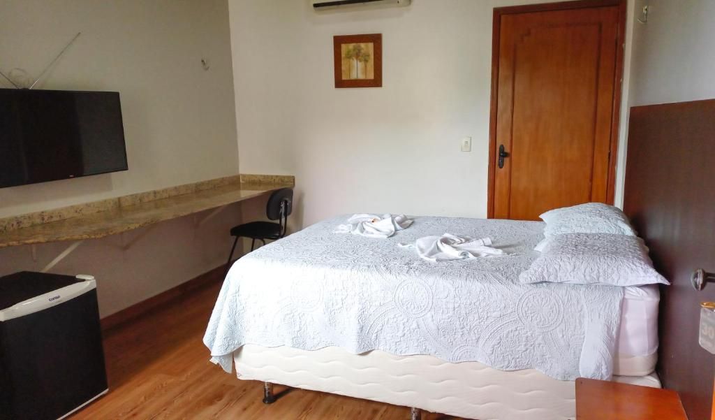 Una camera da letto con un letto, una televisione a muro, una porta in legno e un piccolo cestino nero.