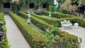 A courtyard with manicured hedges, a statue, and a bench.