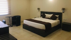 Una habitación de hotel con cama, mesitas de noche, escritorio y ventana con persianas.