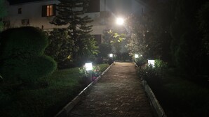 Un sendero nocturno que lleva a un edificio de diseño moderno, rodeado de vegetación cuidada e iluminado con luces pequeñas.