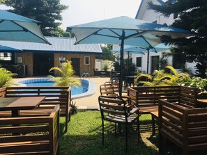 An outdoor pool area with wooden benches and umbrellas, surrounded by greenery and buildings. - Atlantic Hotels and Suites (Lagos)