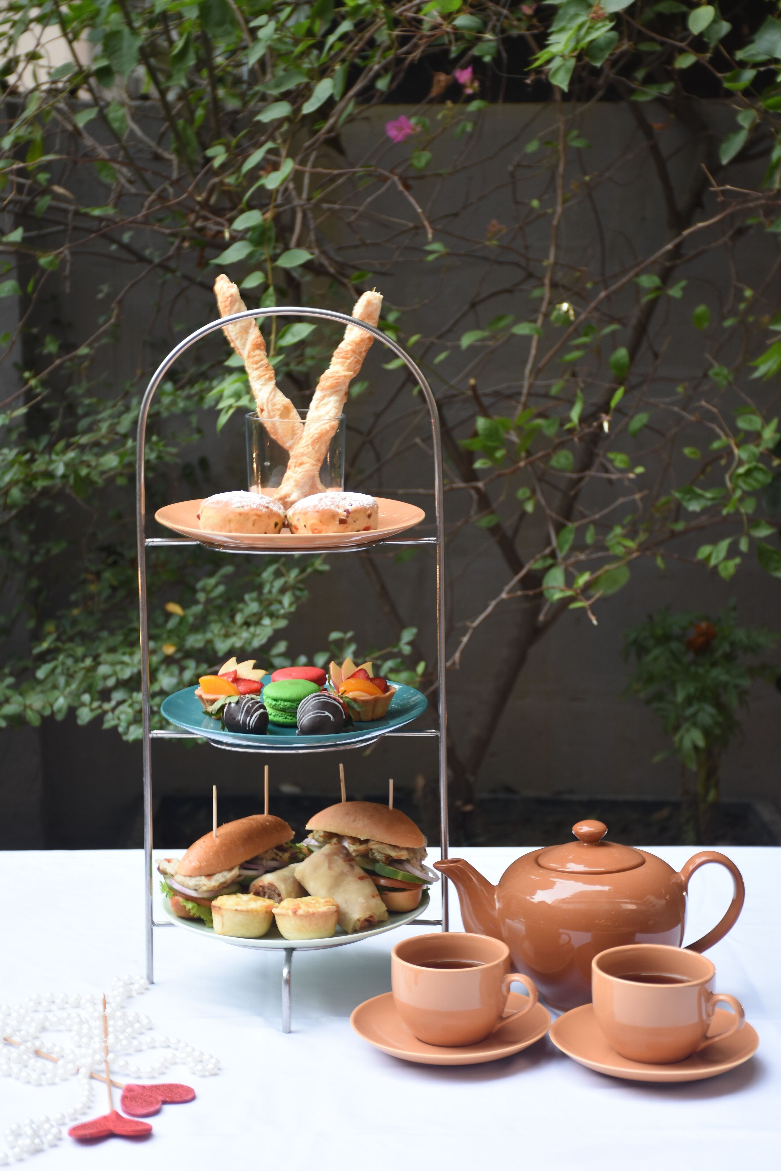 A tiered dessert stand with pastries, a teapot, and cups on a table.