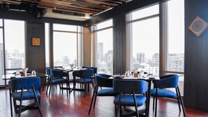 A modern dining area with tables and chairs, large windows with a city view, and a wooden ceiling. - Amari Dhaka (Dhaka)
