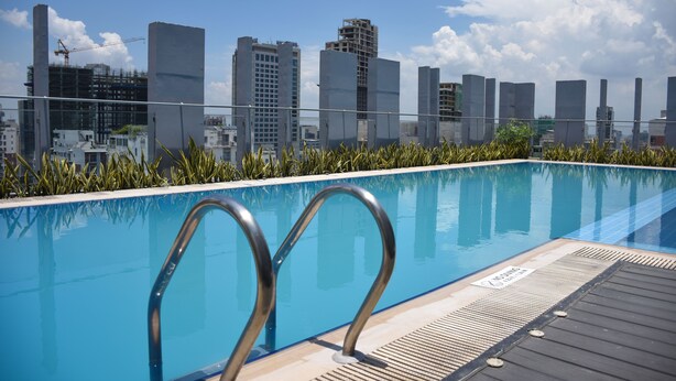 A rooftop pool with metal railings, surrounded by greenery and overlooking a cityscape with modern buildings. - Amari Dhaka (Dhaka)