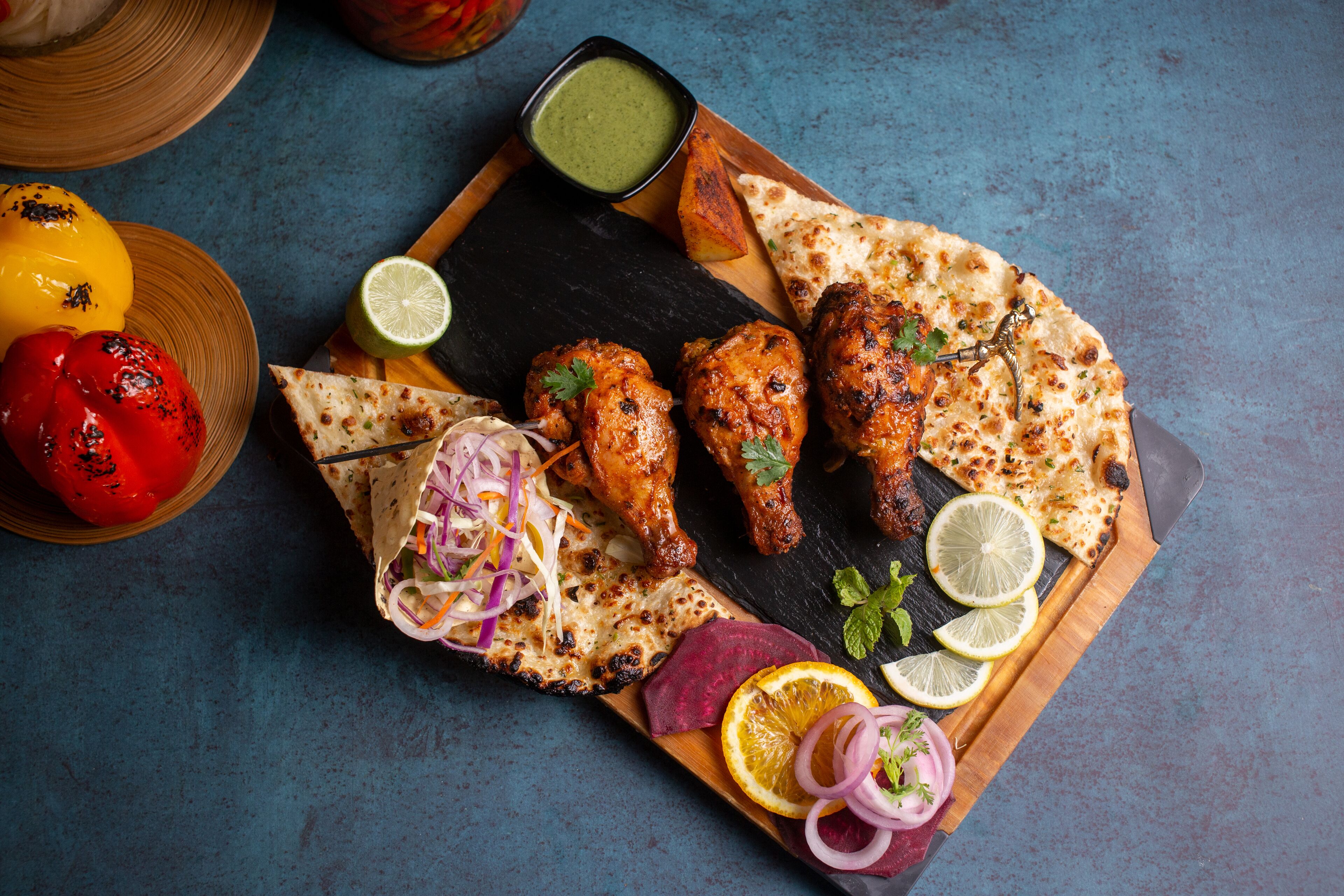 A wooden board with grilled chicken, naan bread, and a side salad.