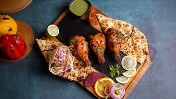 A wooden board with grilled chicken, naan bread, and a side salad.