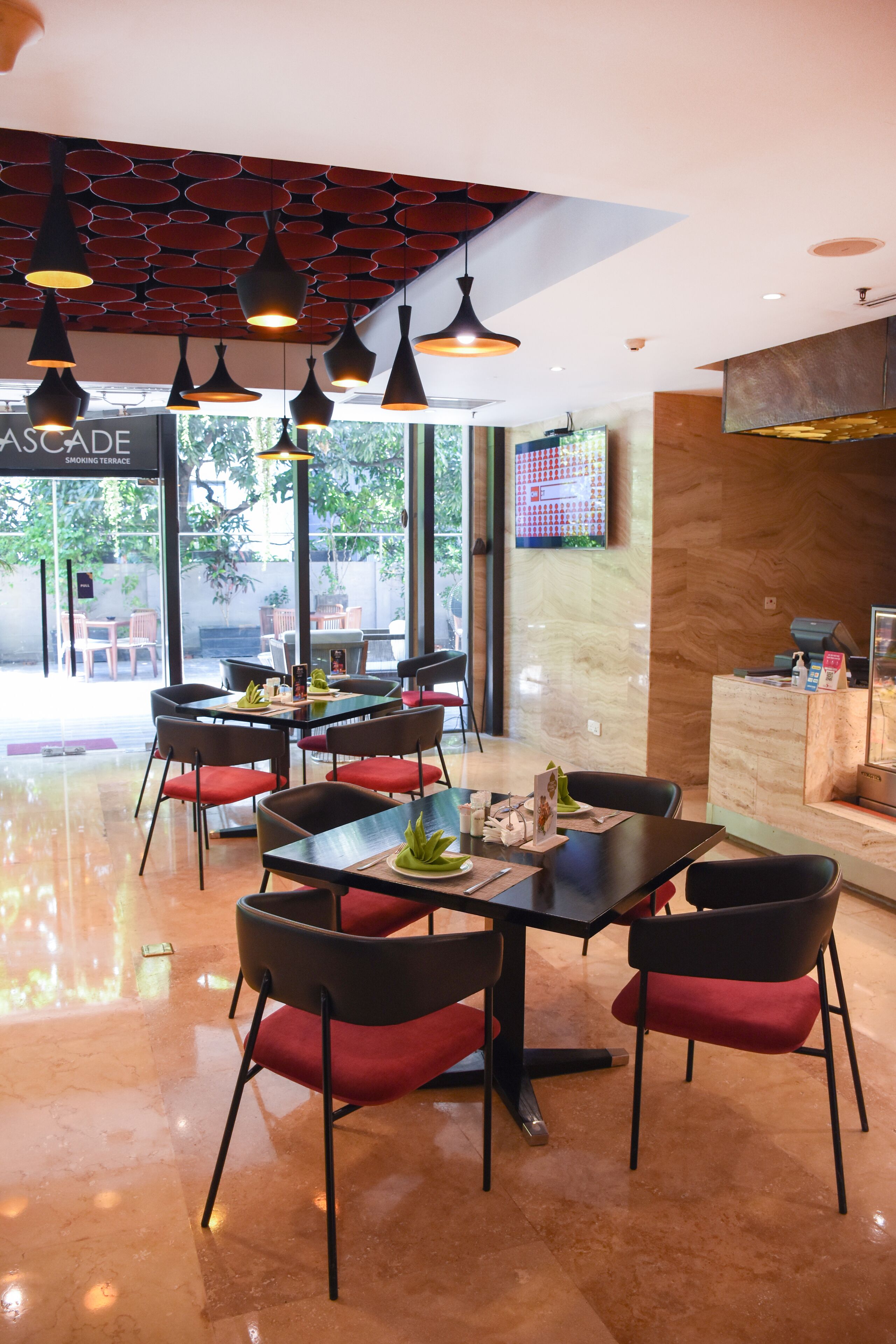 A modern restaurant with a central dining area featuring black tables and red cushioned chairs.