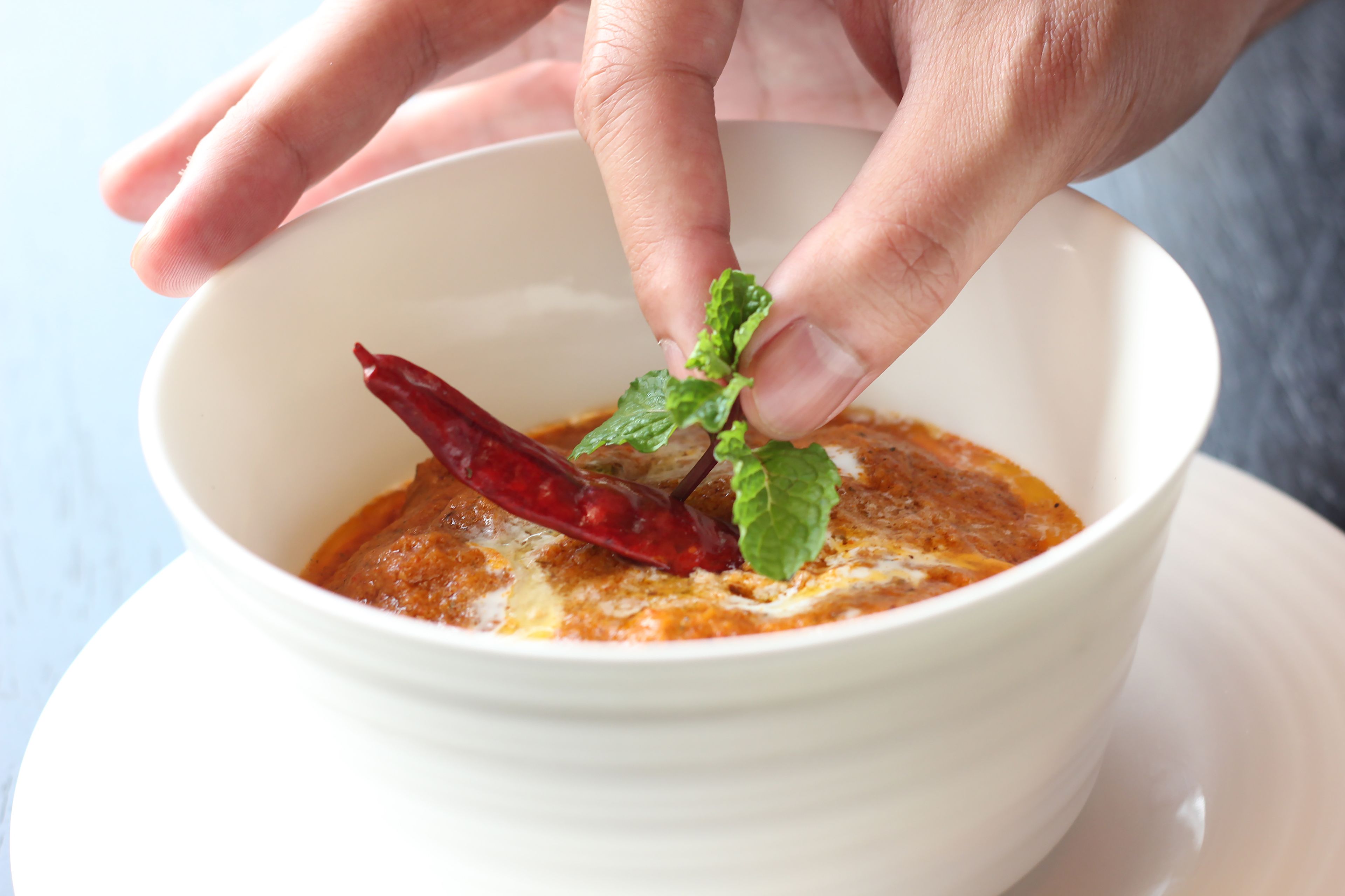 A bowl of soup with a red chili and a mint leaf on top.