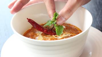 A bowl of soup with a red chili and a mint leaf on top.
