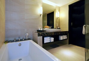Un baño moderno con una bañera grande, un tocador con encimera de mármol, una mampara de cristal y una puerta oscura.