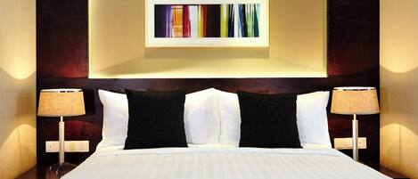 Habitación de hotel con una cama grande, dos mesitas de noche con lámparas, una obra de arte en la pared y un cabecero de madera oscura.
