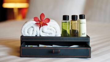 A neatly folded towel with a red flower, two bottles of shampoo, and a bottle of body lotion on a bed.