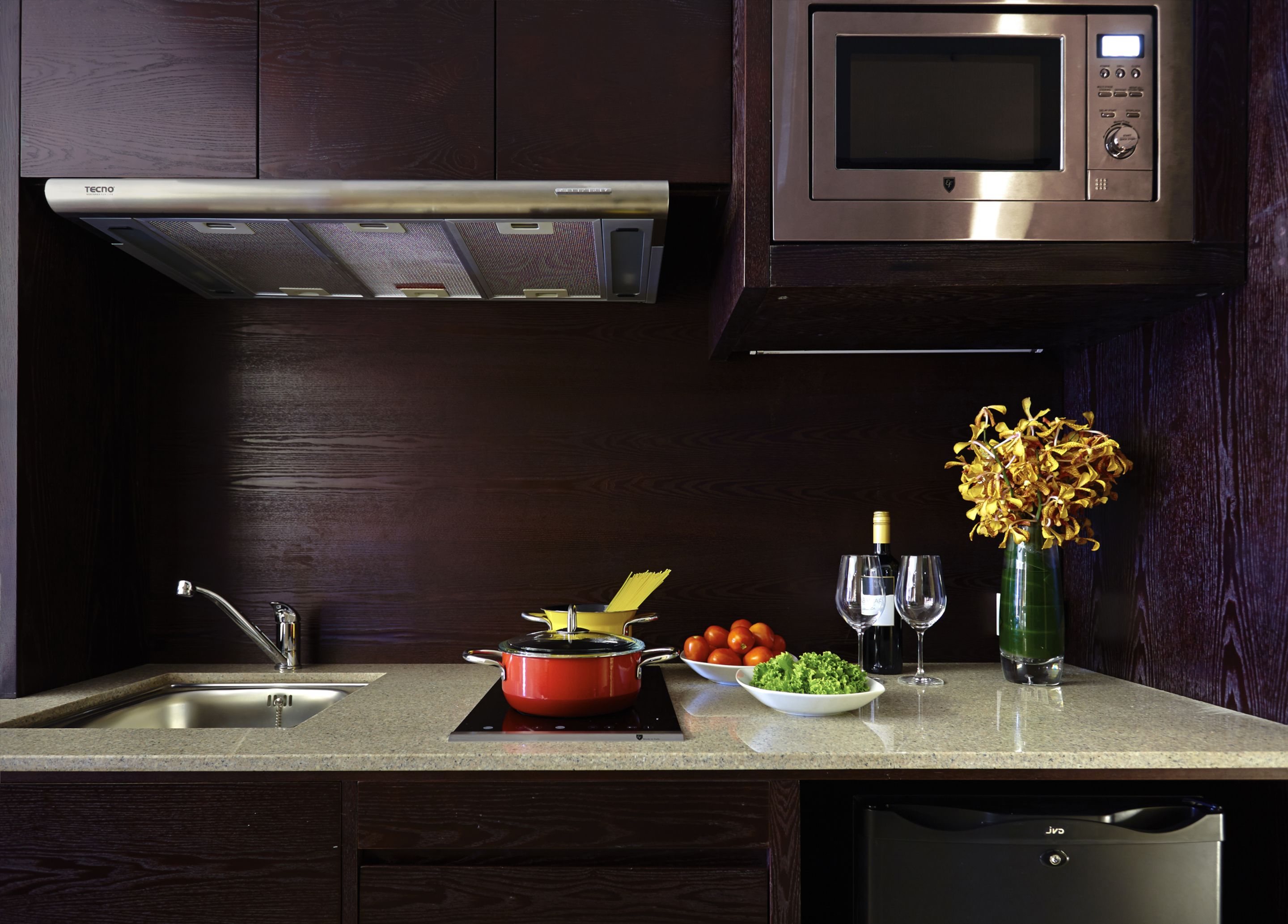A kitchen with a microwave, stove, sink, and a vase with flowers.
