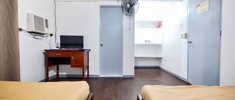 Ett hotellrum med två sängar, ett skrivbord med en dator, en väggmonterad luftkonditioneringsanläggning och en dörr som leder till ett annat rum.