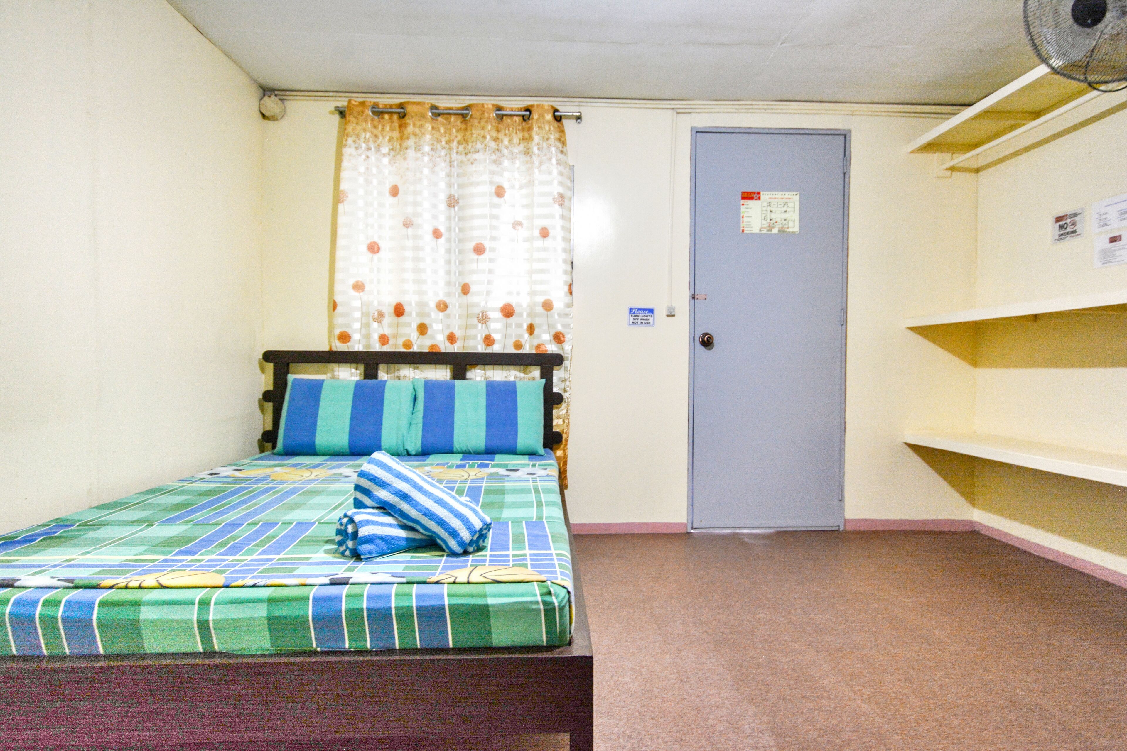 A small, single-bed room with a wooden headboard, a blue door, and a curtain with a polka dot pattern.