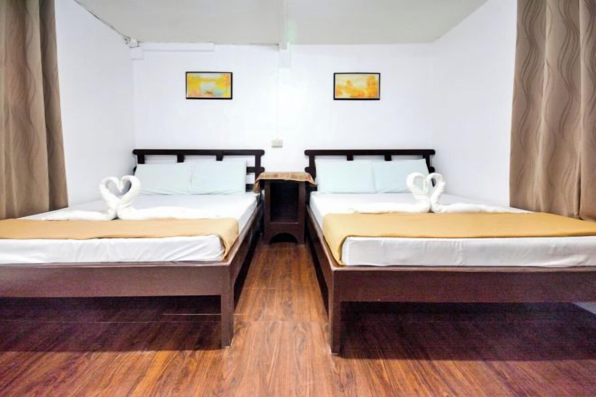 A hotel room with two single beds, wooden flooring, and two framed pictures on the wall.