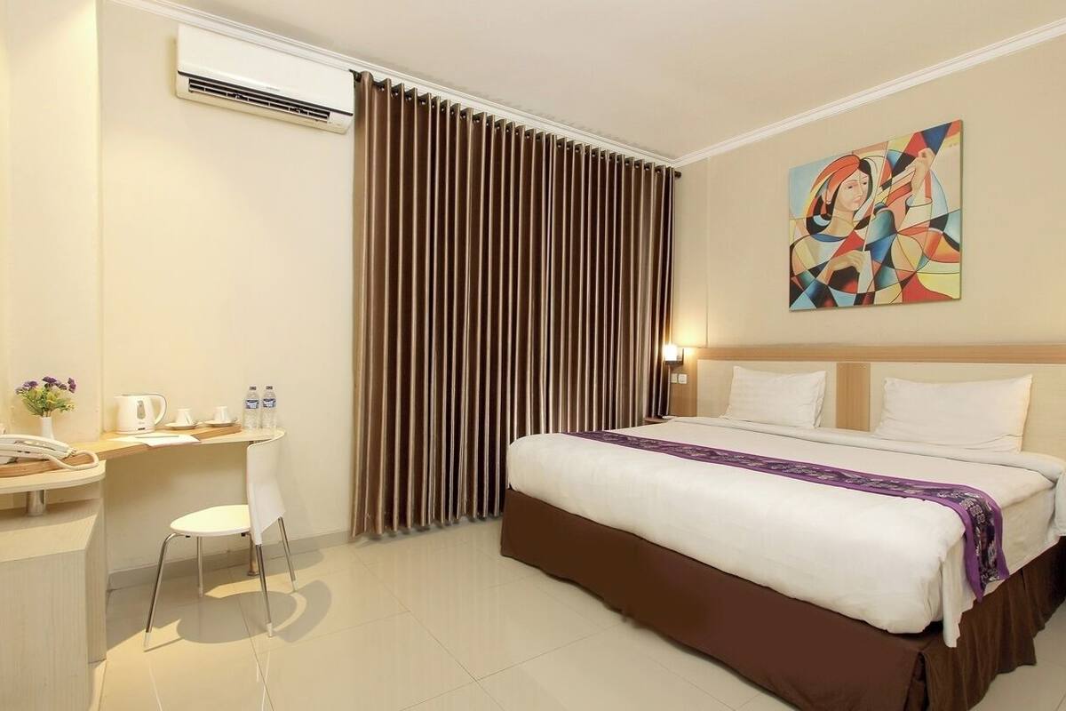 Une chambre d’hôtel avec un lit, un bureau, une chaise, un climatiseur et un tableau au mur.