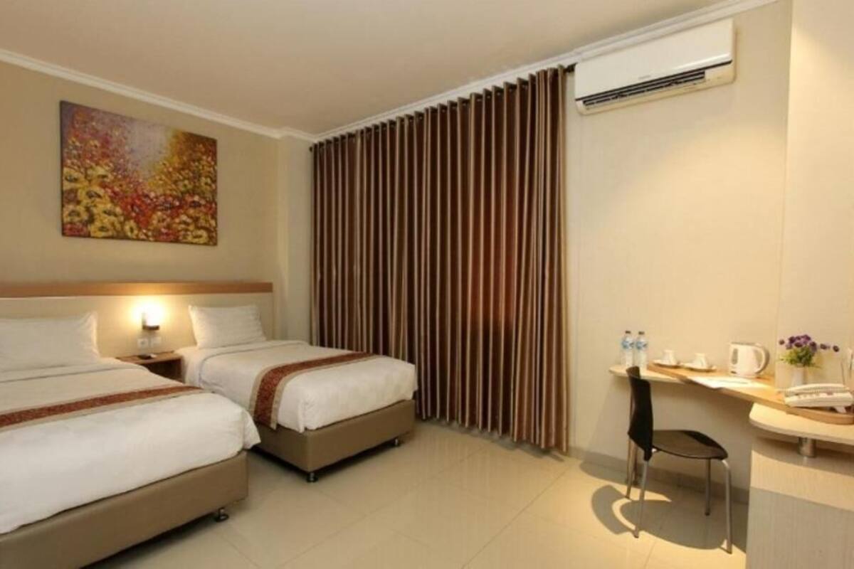 Une chambre d’hôtel avec deux lits, un bureau, une chaise, un appareil de climatisation et un tableau au mur.