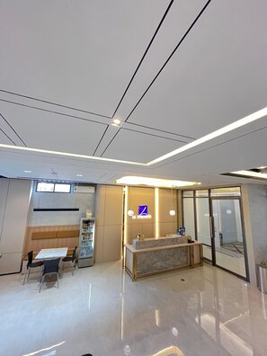 A modern hotel lobby with a reception desk, seating area, and a vending machine. - Laxston Hotel by Front One (Yogyakarta)