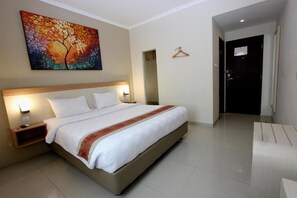A hotel room with a large bed, bedside tables, a painting on the wall, and a door to the right. - Laxston Hotel by Front One (Yogyakarta)