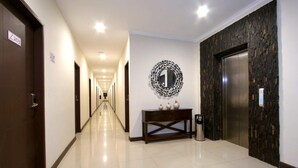 A hotel hallway with a long corridor, an elevator, a wall-mounted mirror, and a console table with decorative items. - Laxston Hotel by Front One (Yogyakarta)