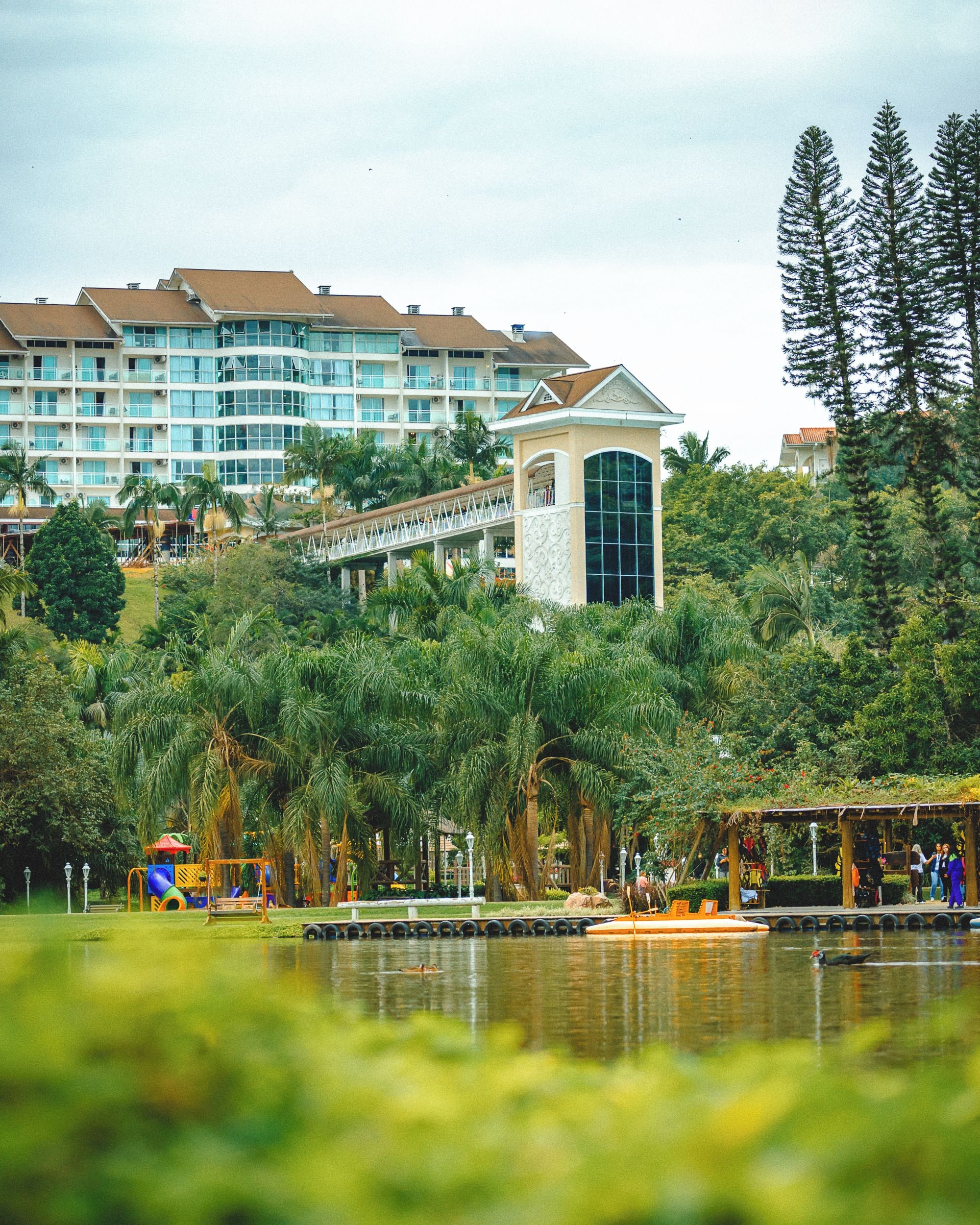 Un hotel con varias construcciones, una torre y un parque con un lago.