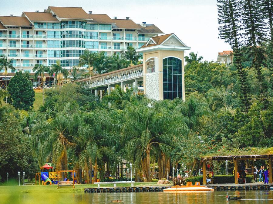 Un hotel con varias construcciones, una torre y un parque con un lago.