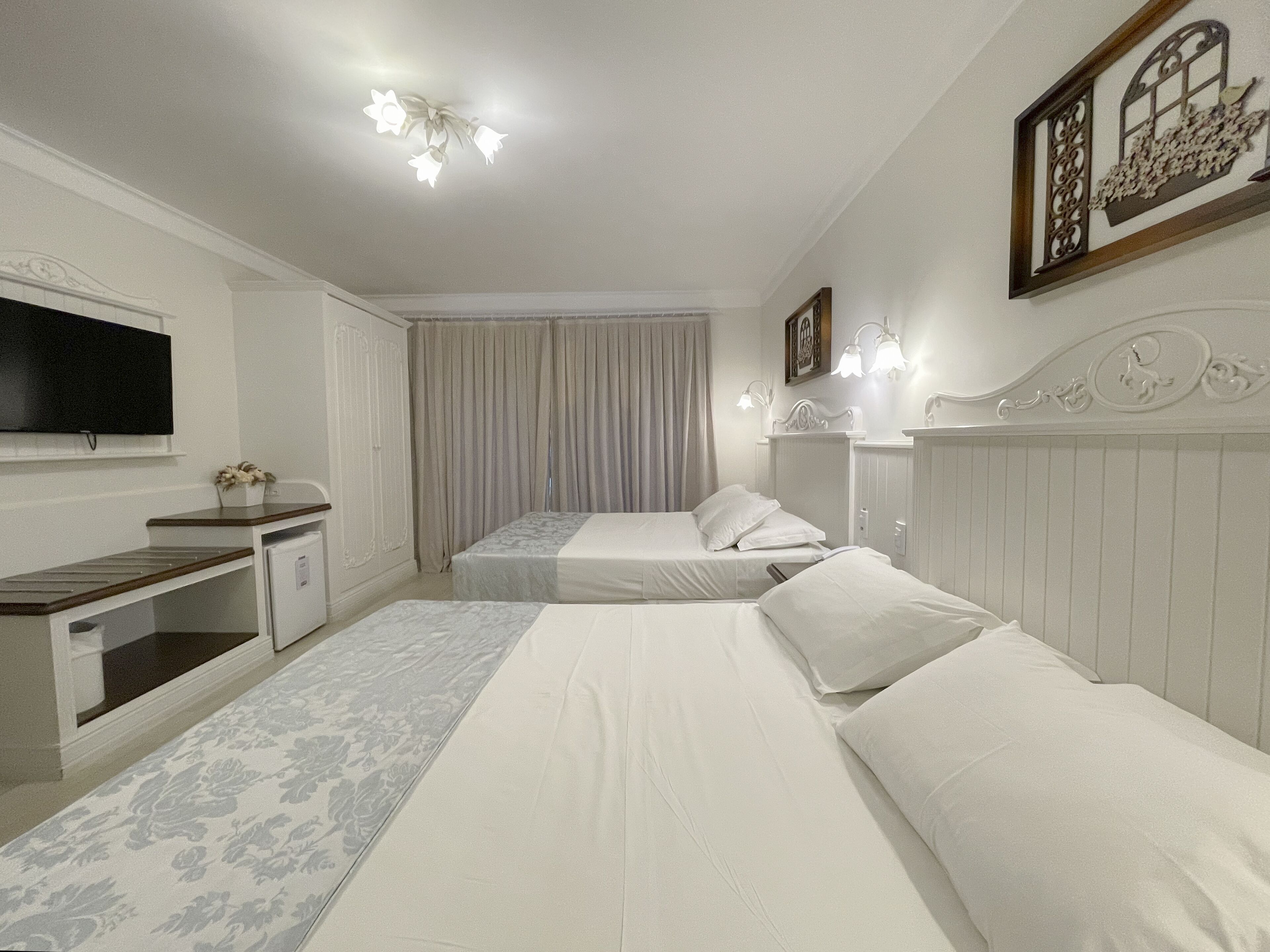 Quarto de hotel com duas camas, televisão, escrivaninha e janela com cortinas.
