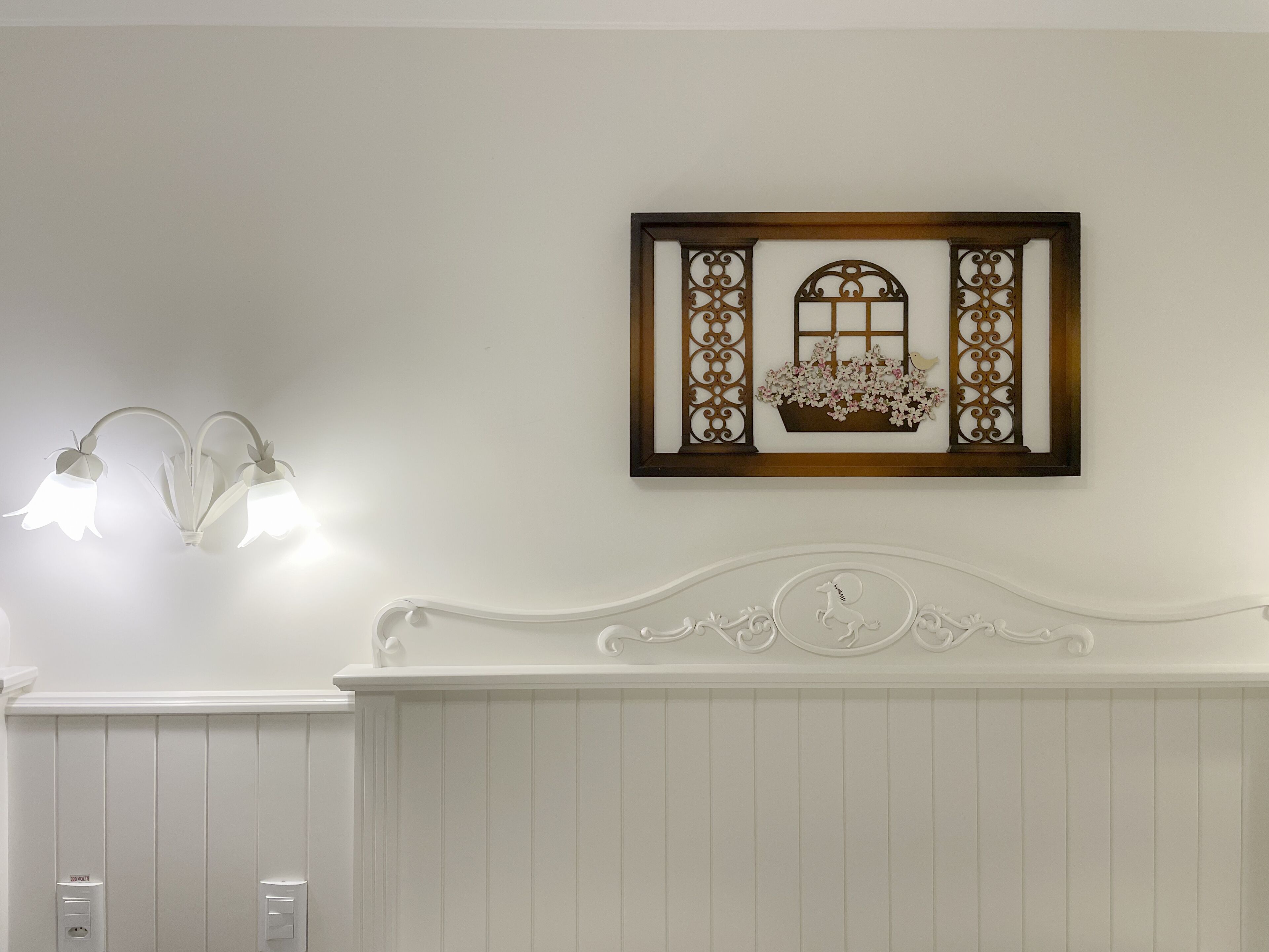 A bathroom with a white vanity, a wall-mounted light fixture, and a decorative piece above the mirror.