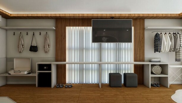 A modern room with a wooden ceiling, a large window with blinds, a flat-screen TV mounted on the wall, a white desk, a chair, a coat rack with hanging clothes, and a shoe rack with shoes. - Fazzenda Park Resort (Gaspar)