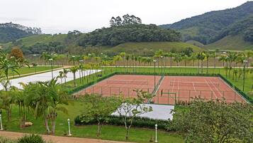 A tennis court surrounded by greenery and palm trees.
