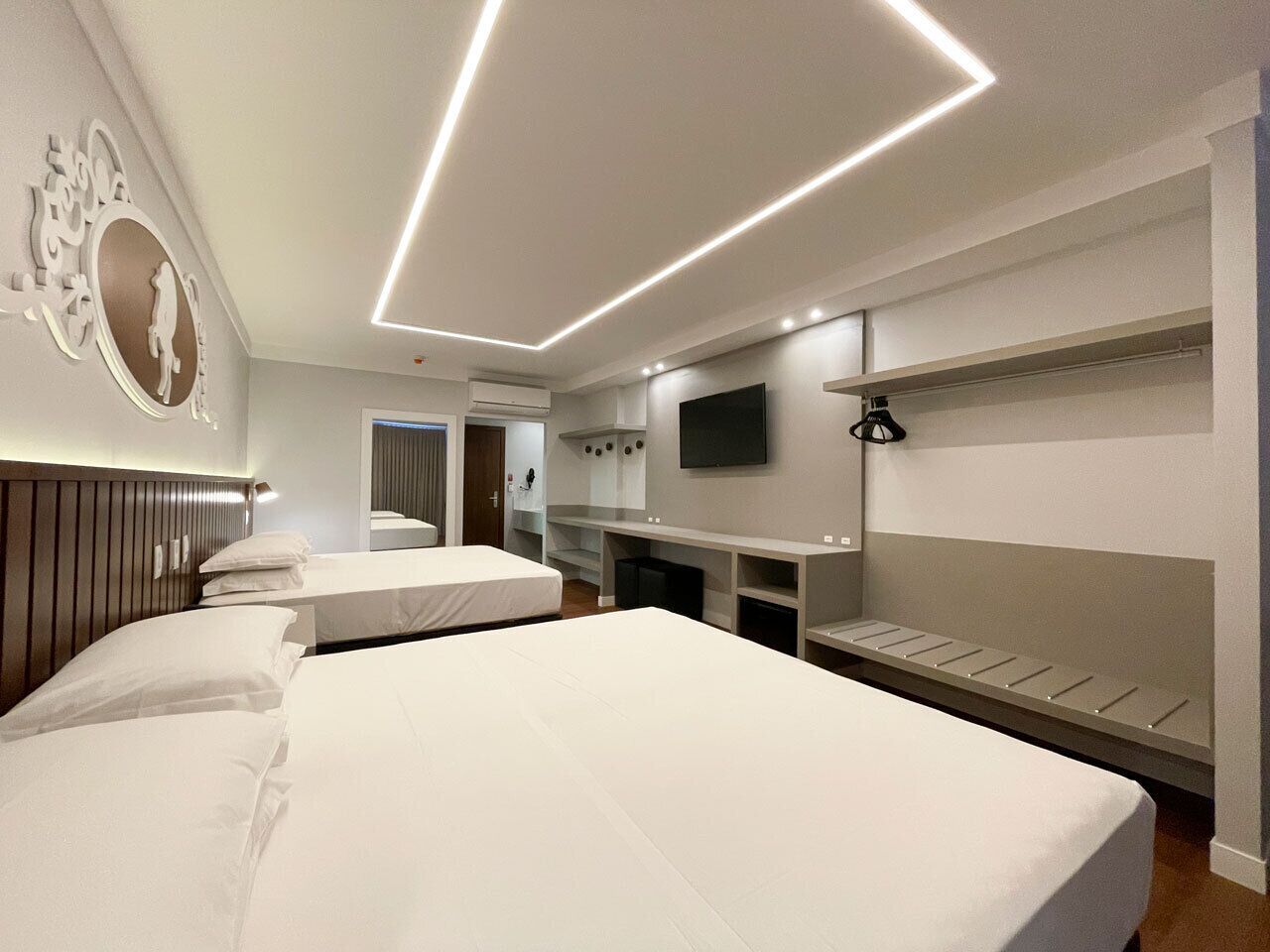 Quarto de hotel com duas camas, uma televisão, uma escrivaninha e um espelho.