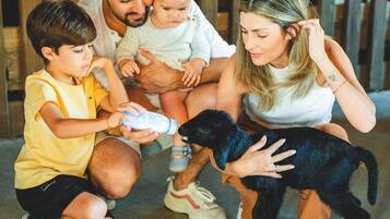 Una familia con un cachorro en un espacio al aire libre cubierto, con una valla de madera.