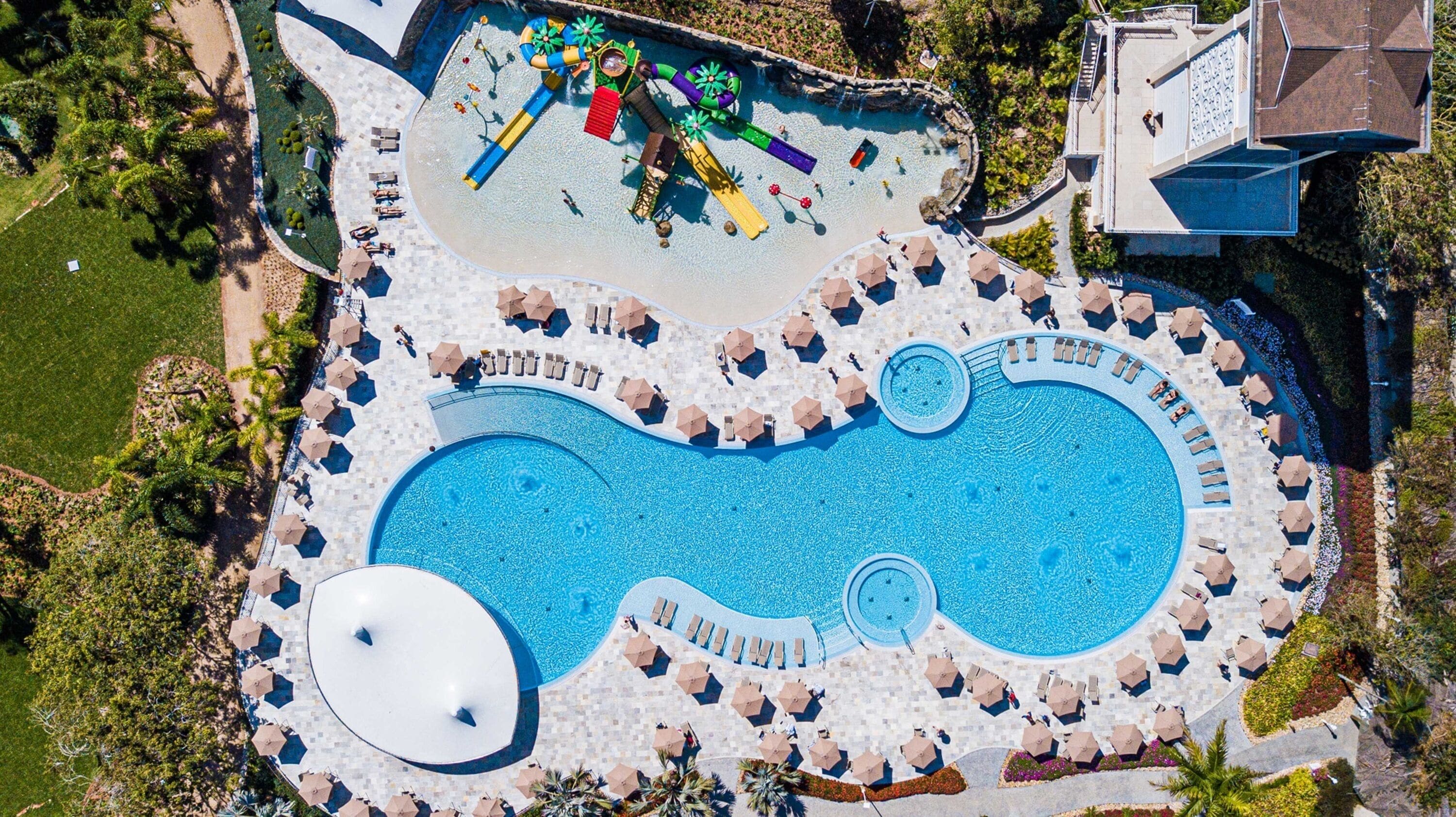 An aerial view of a resort with a large central pool, multiple smaller pools, and a water park area.