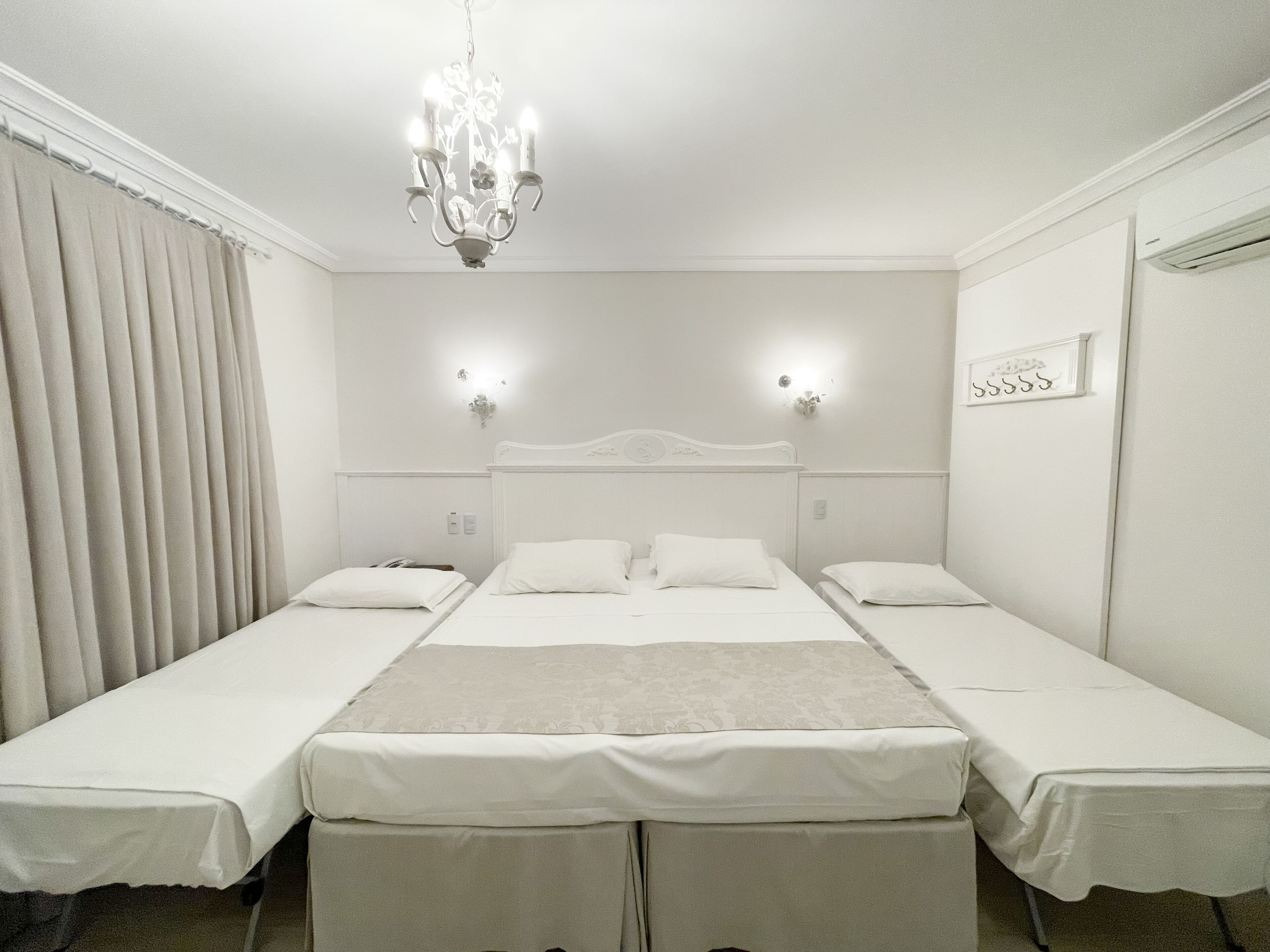 Quarto de hotel com duas camas de solteiro, um candelabro, arandelas e um quadro na parede.