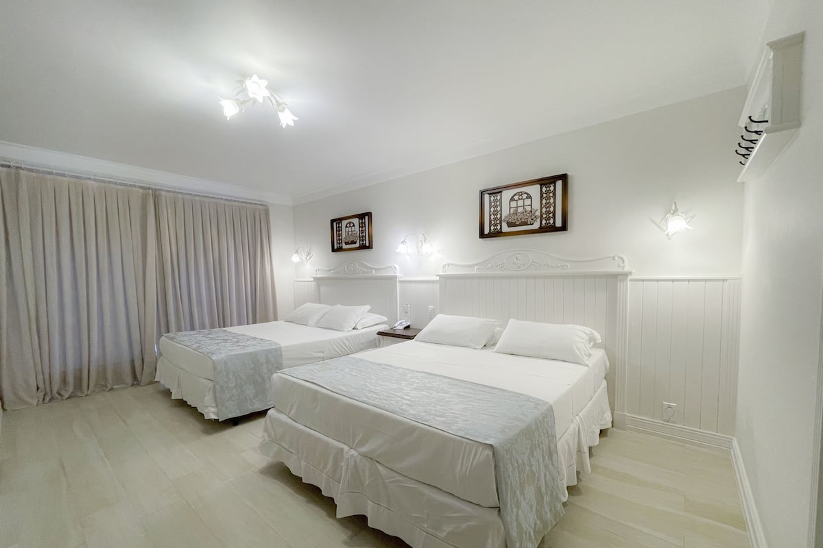 A hotel room with two beds, a large window with curtains, a chandelier, and wall-mounted artwork.