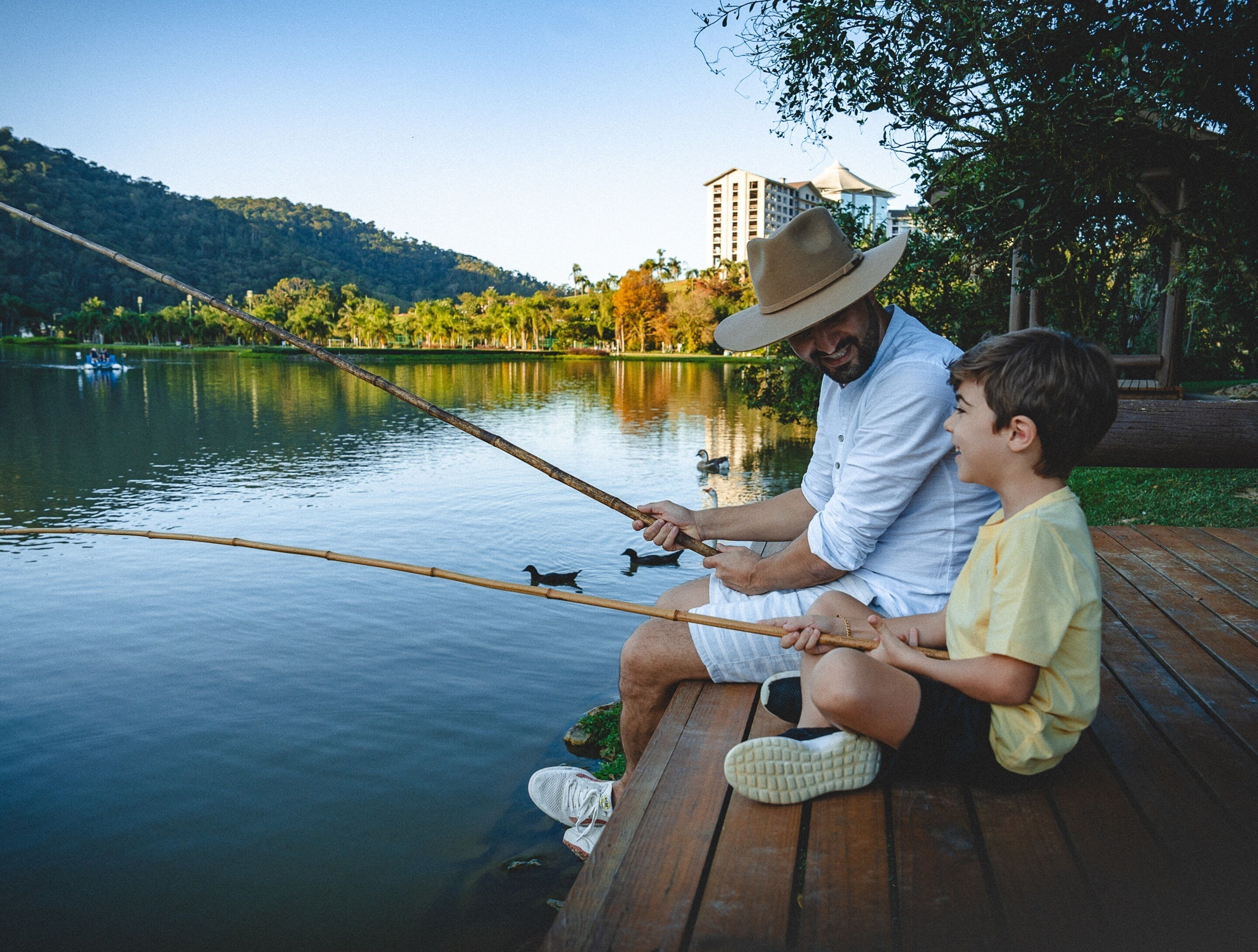 Un hombre y un niño sentados en un muelle de madera junto a un lago, pescando.