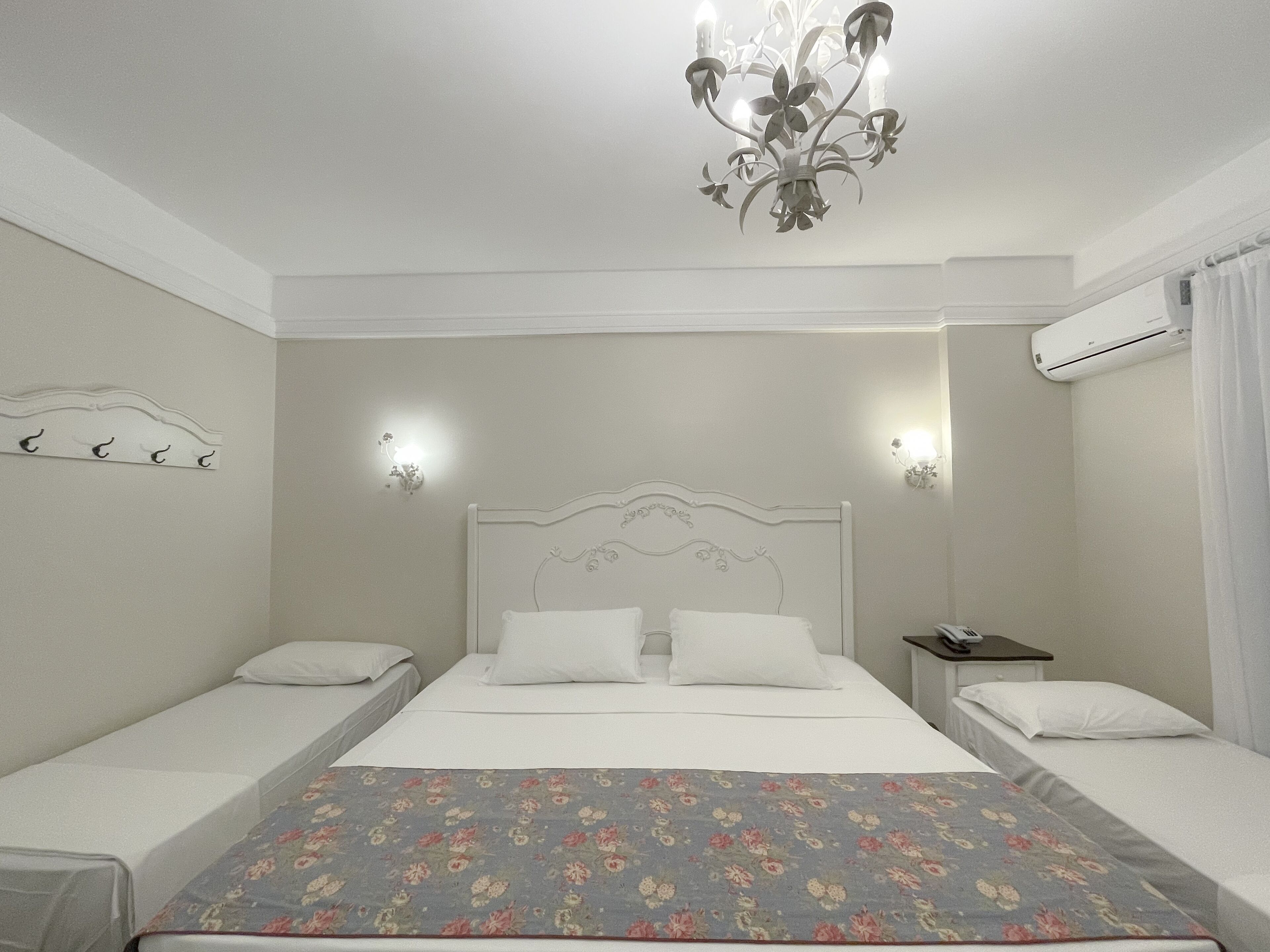 Habitación de hotel con una cama grande, dos mesitas de noche, un candelabro, apliques de pared y un equipo de aire acondicionado.