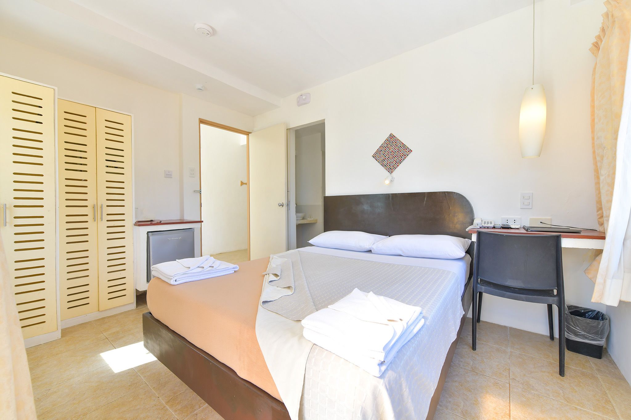 Une chambre d’hôtel comprenant un lit, un bureau, une chaise, une armoire et une petite table.