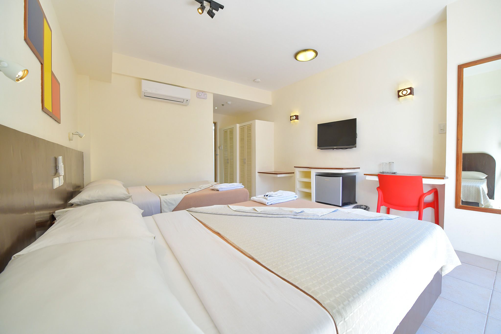 Habitación de hotel con dos camas, un escritorio, un televisor y un espejo.