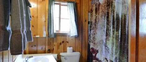 A wooden bathroom with a white sink, toilet, and shower curtain with a forest print.
