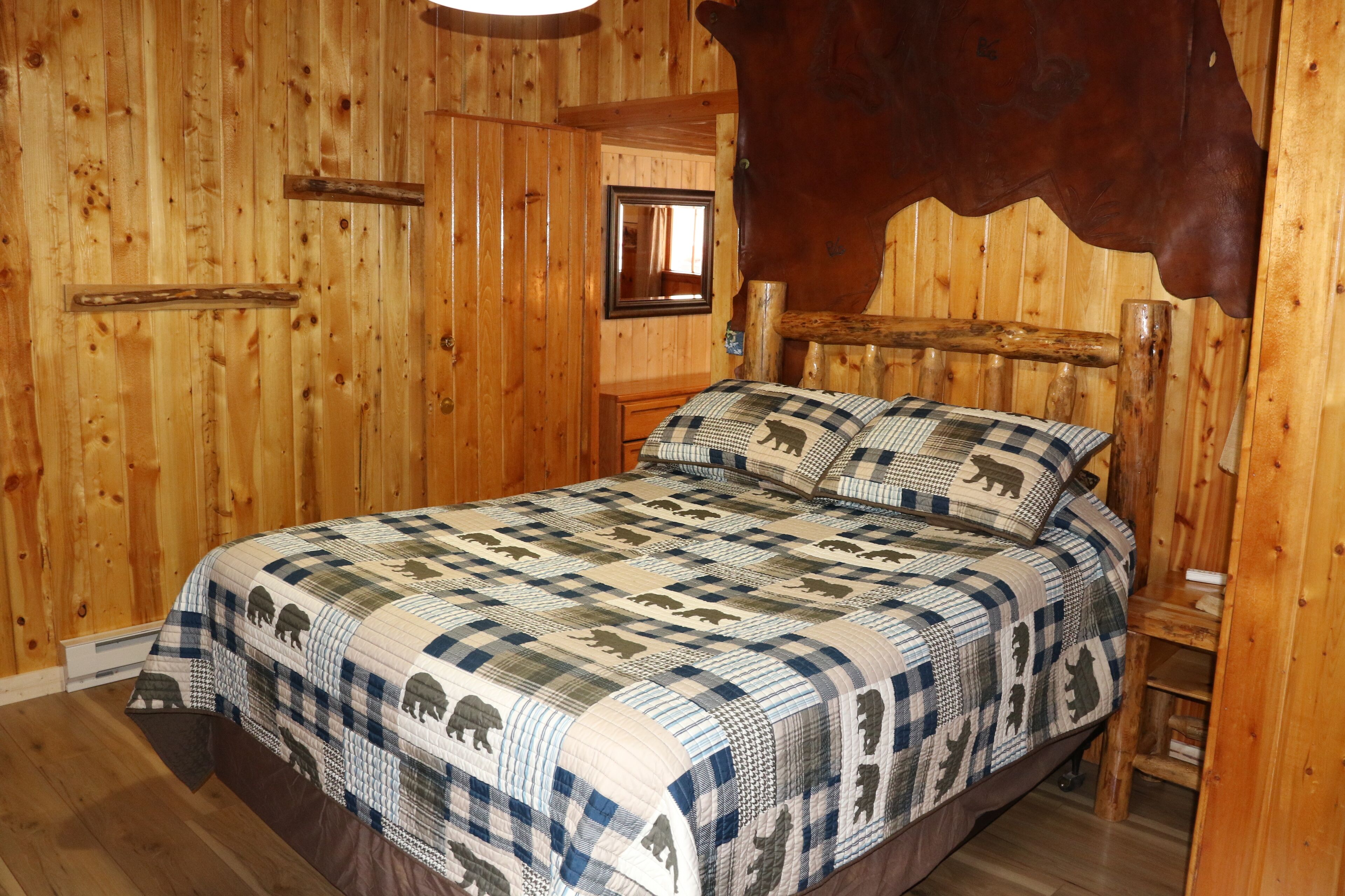 Una habitación de madera con una cama que presenta un plaid con estampados de animales, un cabecero de madera y una cabeza de animal montada.