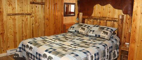 Una habitación de madera con una cama que presenta un plaid con estampados de animales, un cabecero de madera y una cabeza de animal montada.