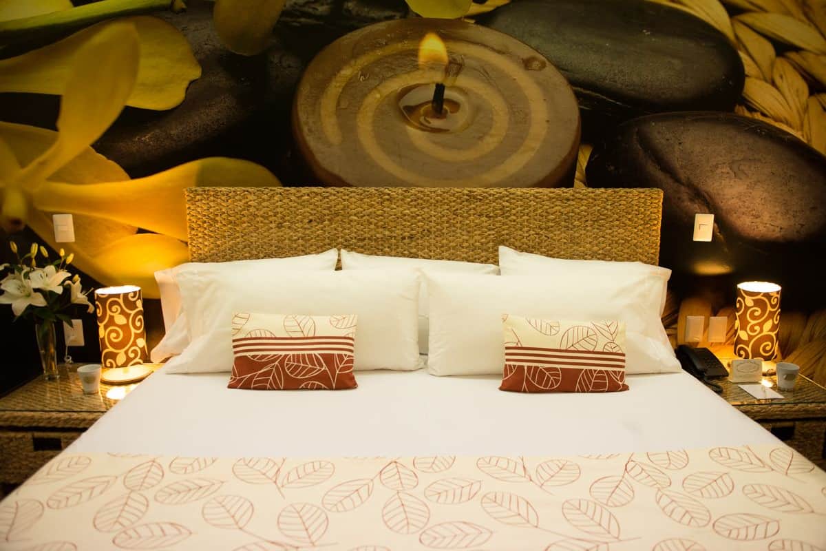 A neatly made bed with white linens and patterned pillows, a textured headboard, and a decorative wall with a circular design.